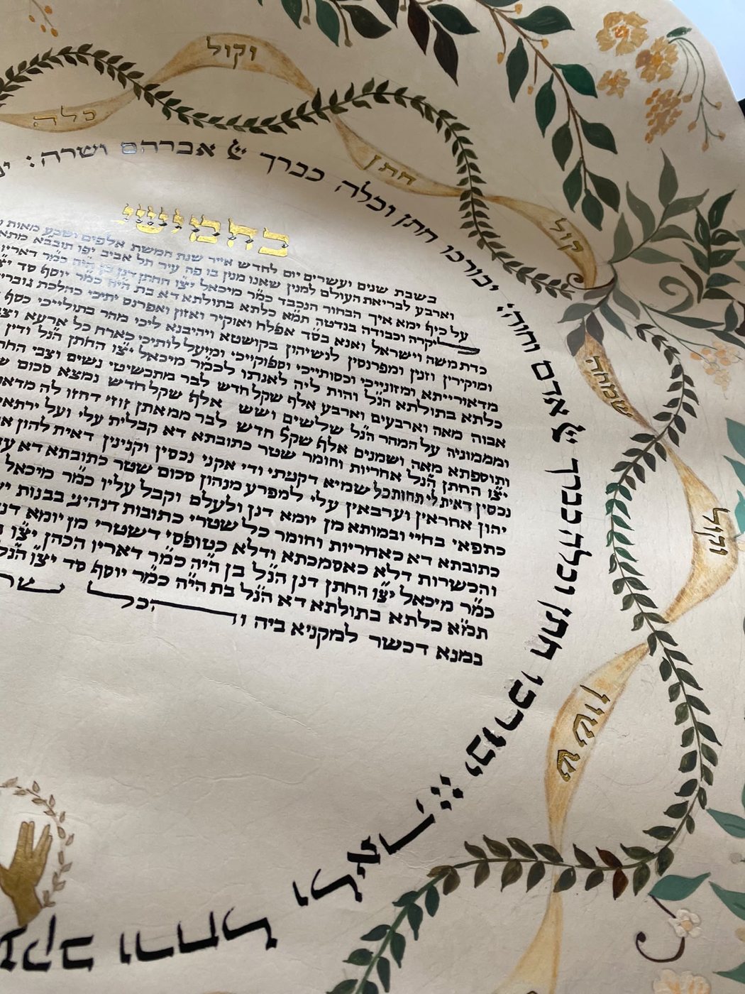 Nel dettaglio laterale, la scrittura arcuata incontra i nastri dorati e le ghirlande: tre linee ornamentali diverse si rincorrono senza perdere leggibilità.