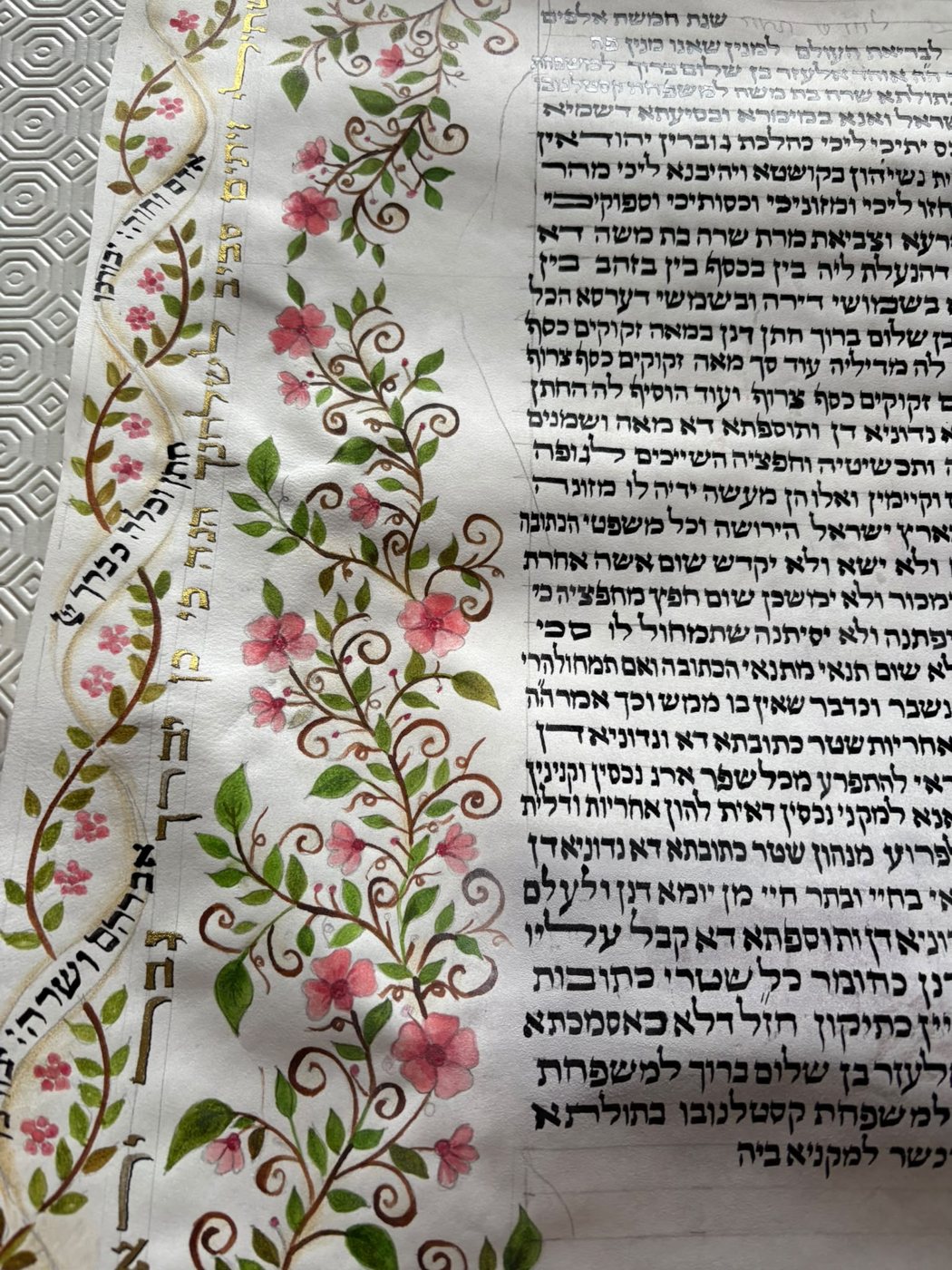 Il bordo sinistro si rivela come un intreccio di steli, foglie appuntite e fiori rosati; la scrittura compatta ne accentua la leggerezza ornamentale.