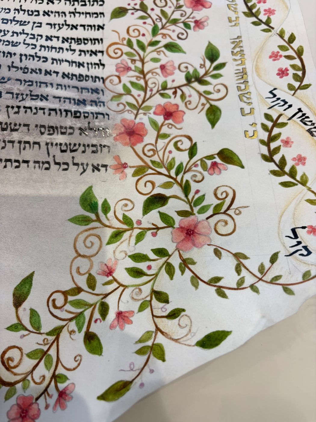 Nella zona inferiore, i rami si raccolgono in un motivo ricurvo: i particolari dorati e i fiori rosa accompagnano l’iscrizione lungo la sagoma.